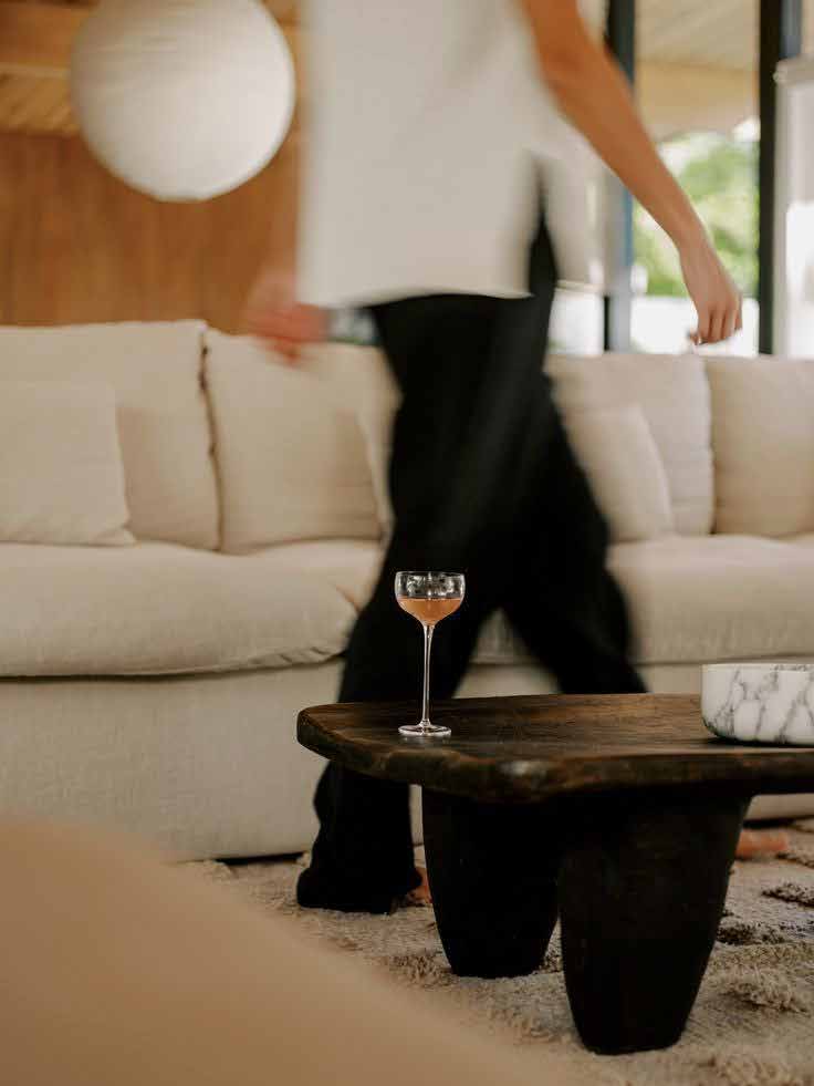 Invitada caminando junto a una sala clara con copa sobre la mesa